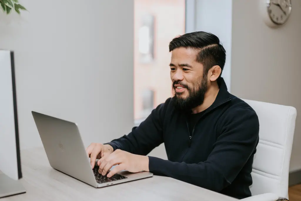 A man sitting at a computer in an office as he creates mentoring program matches using a template.