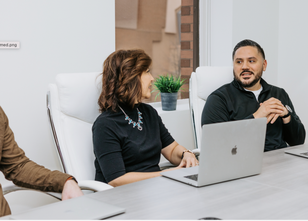 Two employees sitting in an diverse workplace setting having a conversation.