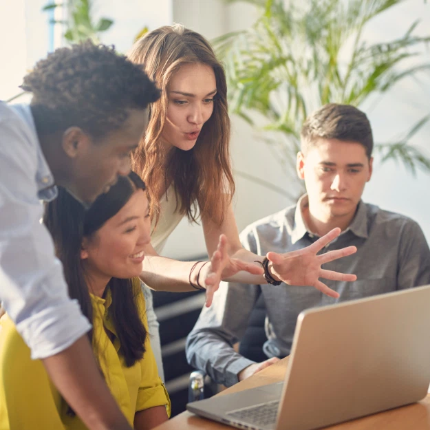 Coworkers collaborating around a laptop during a team discussion in a bright office.