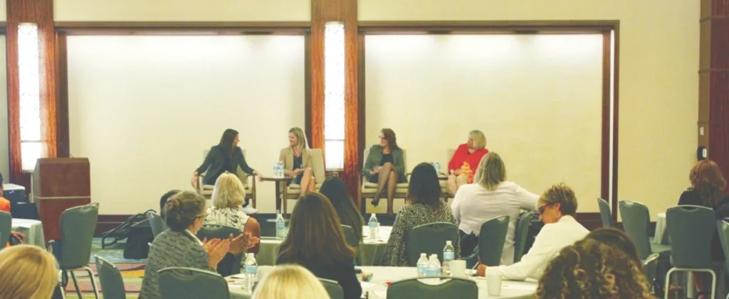 Women participating in a panel discussion in front of an audience at a professional conference or leadership event.