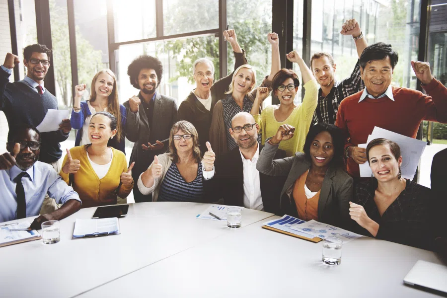 Diverse group of coworkers celebrating together around a conference table in a bright office.